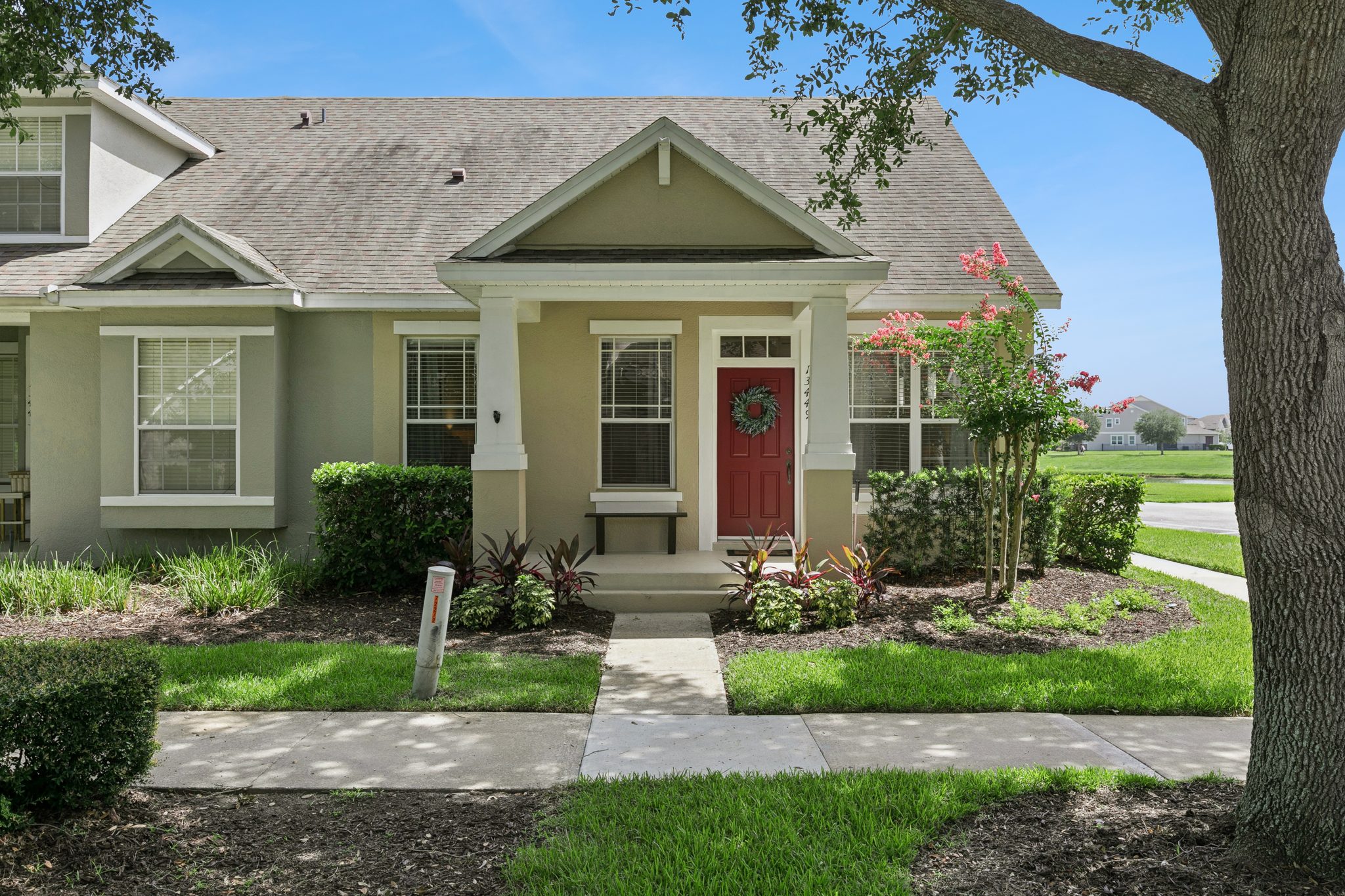 Front exterior of 13449 Carroway St — a renovated two-story townhome in Windermere's Merrick Landing with a covered entry, red front door, and mature oak-and-palm landscaping